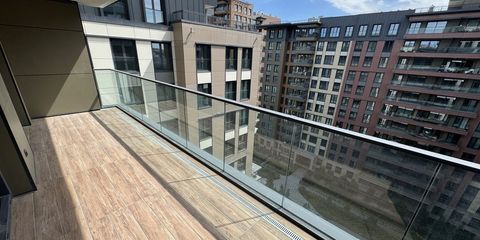 Ahşap görünümlü seramikle kaplı geniş balkon; cam korkuluğun ardında sitenin diğer blokları