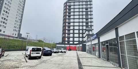 Zemin katında vitrinli dükkânlar bulunan çok katlı bir konut kulesi ve önündeki taş döşeli otopark avlusu