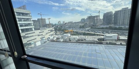 Bir pencereden dışarı bakış; aşağıda teras çatı ve otopark, ufukta inşaat vinçleriyle yükselen binalar