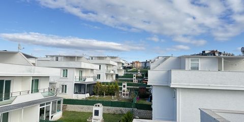 Rows of white detached houses with balconies and green gardens under a blue sky, seen from an upper terrace
