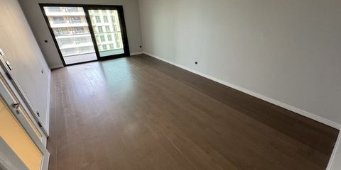 Boş bir dairenin geniş, ahşap parkeli odası; uçtaki balkon kapısından karşı blok görünüyor