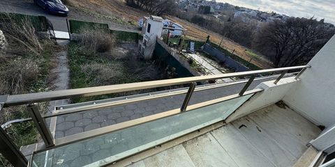 A balcony with a steel railing above an overgrown garden plot, houses spread across the hillside beyond