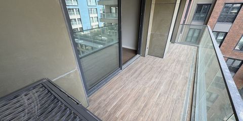 A narrow apartment balcony with wood-effect tiles, neighbouring blocks beyond the glass balustrade