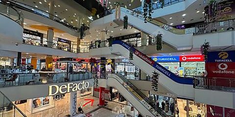 Çok katlı bir alışveriş merkezinin iç görünümü; yürüyen merdivenler ve katlar boyunca sıralanmış mağaza tabelaları