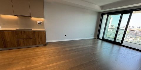 Boş bir dairenin salonu ve açık mutfağı; sürme cam kapıdan balkona ve şehre bakış